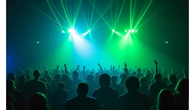 A massive indoor stage filled with fog and powerful green laser beams cutting through the air above a dense crowd.